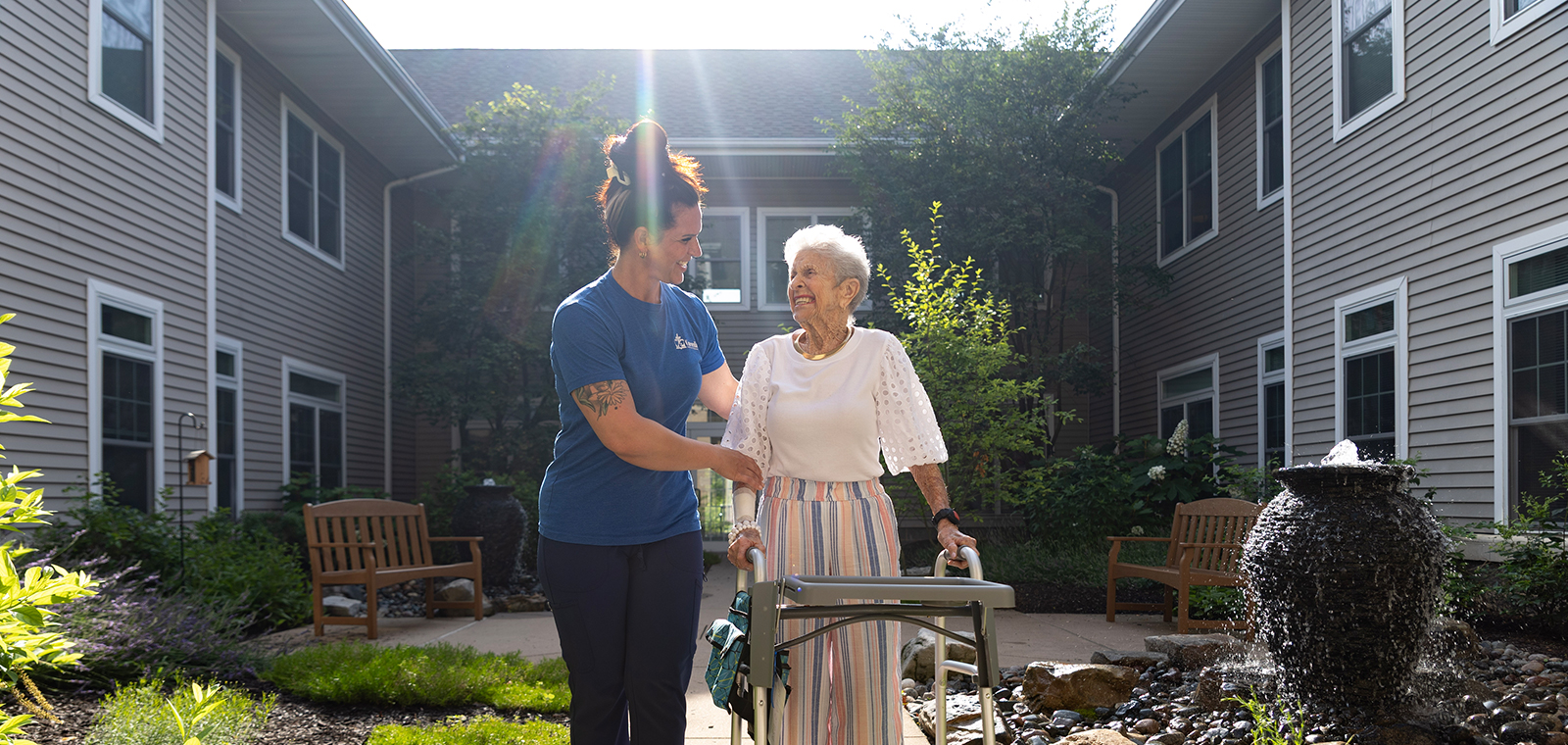 Caregiver assisting elderly woman in a peaceful outdoor setting.