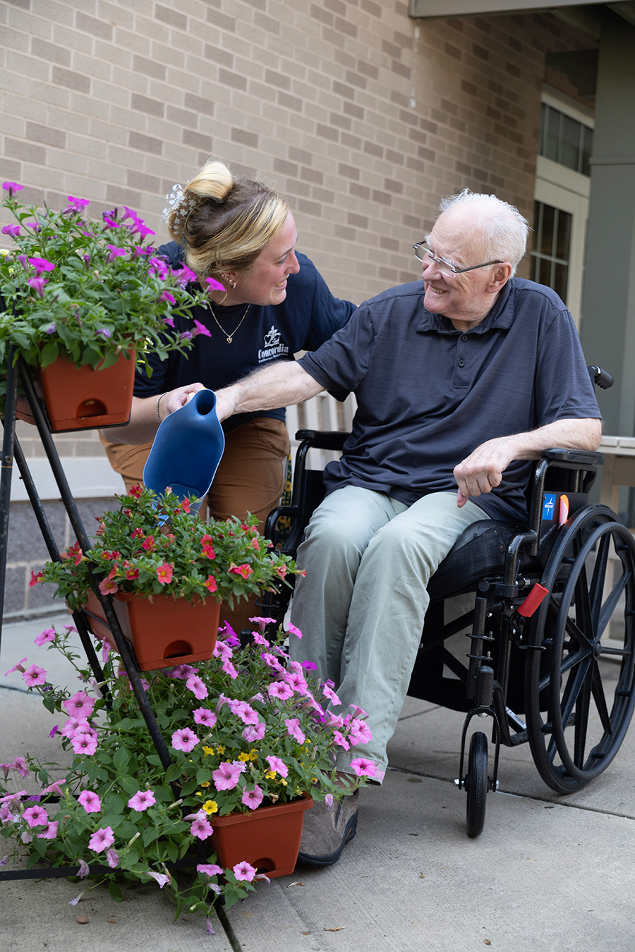 Two people interacting joyfully by potted flowers outdoors.