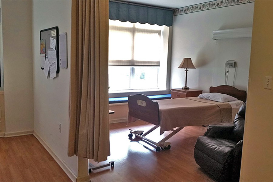 Hospital room with bed, chair, lamp, and window.