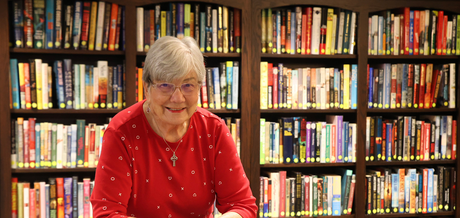 Smiling woman in red shirt, surrounded by bookshelves.
