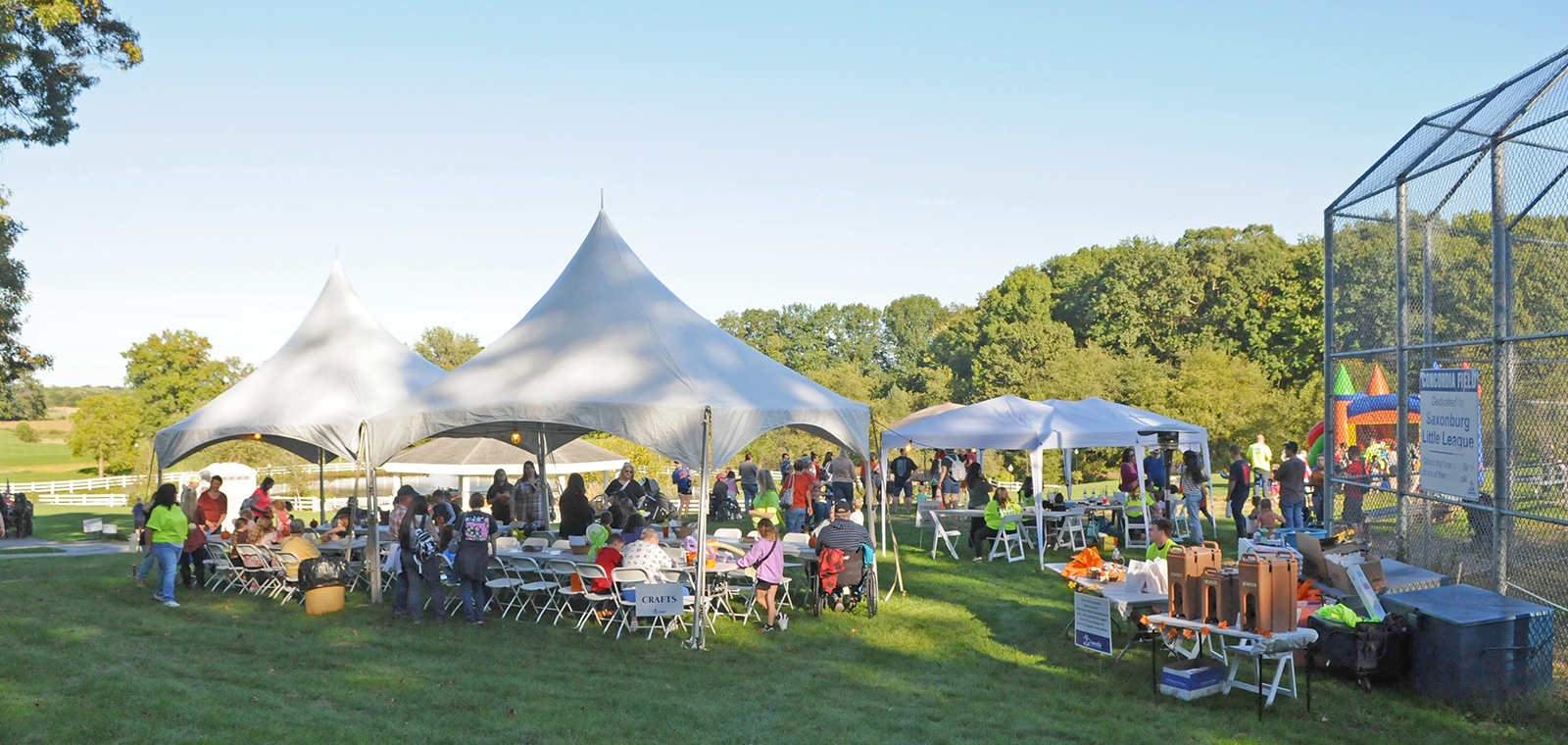 Community event with tents, tables, and many attendees outdoors.