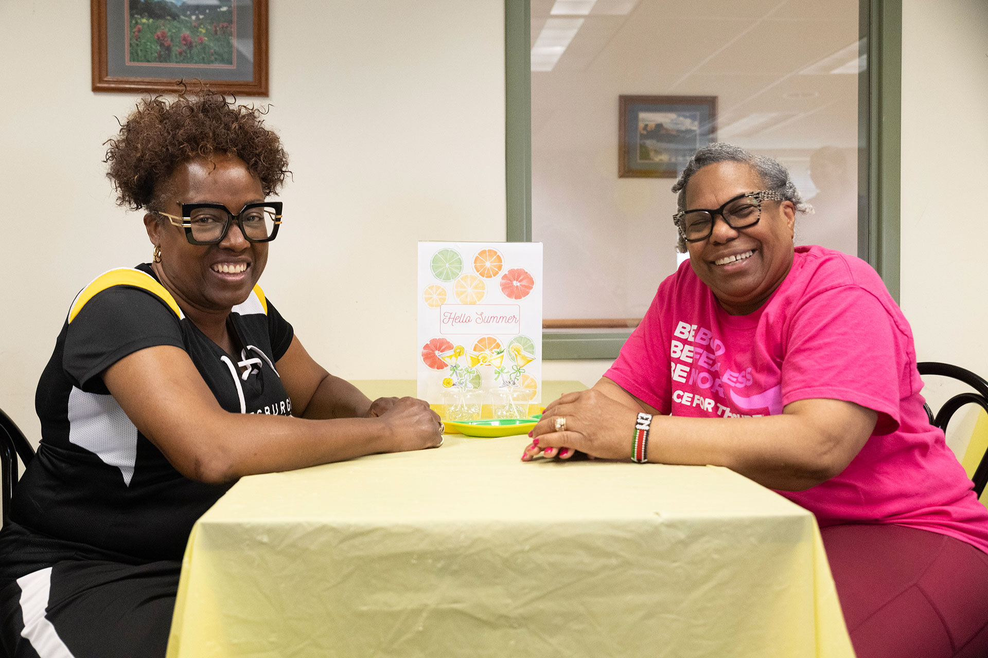 Two smiling women at a table with summer decor.