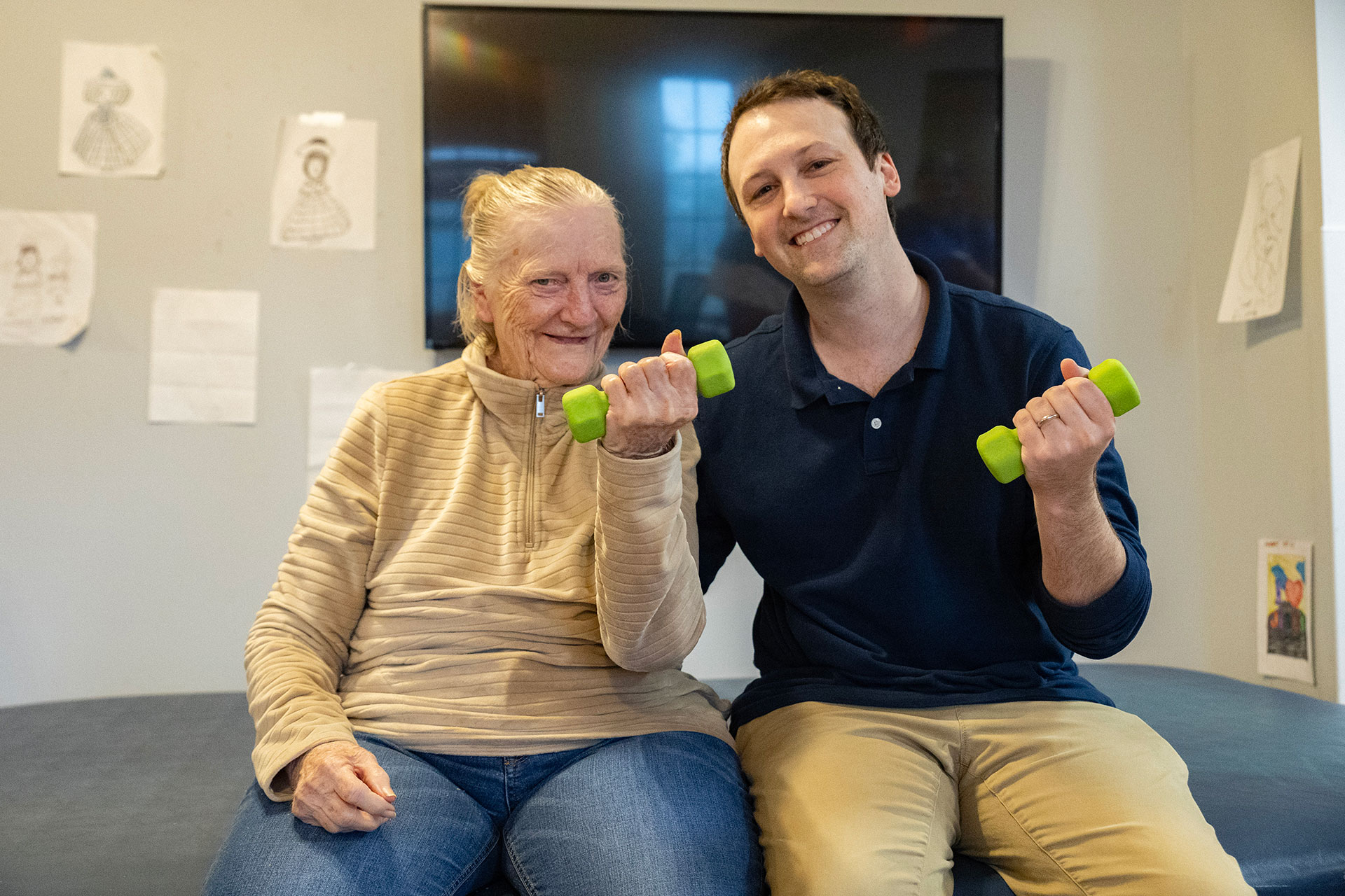 Elderly woman and young man smiling with dumbbells.