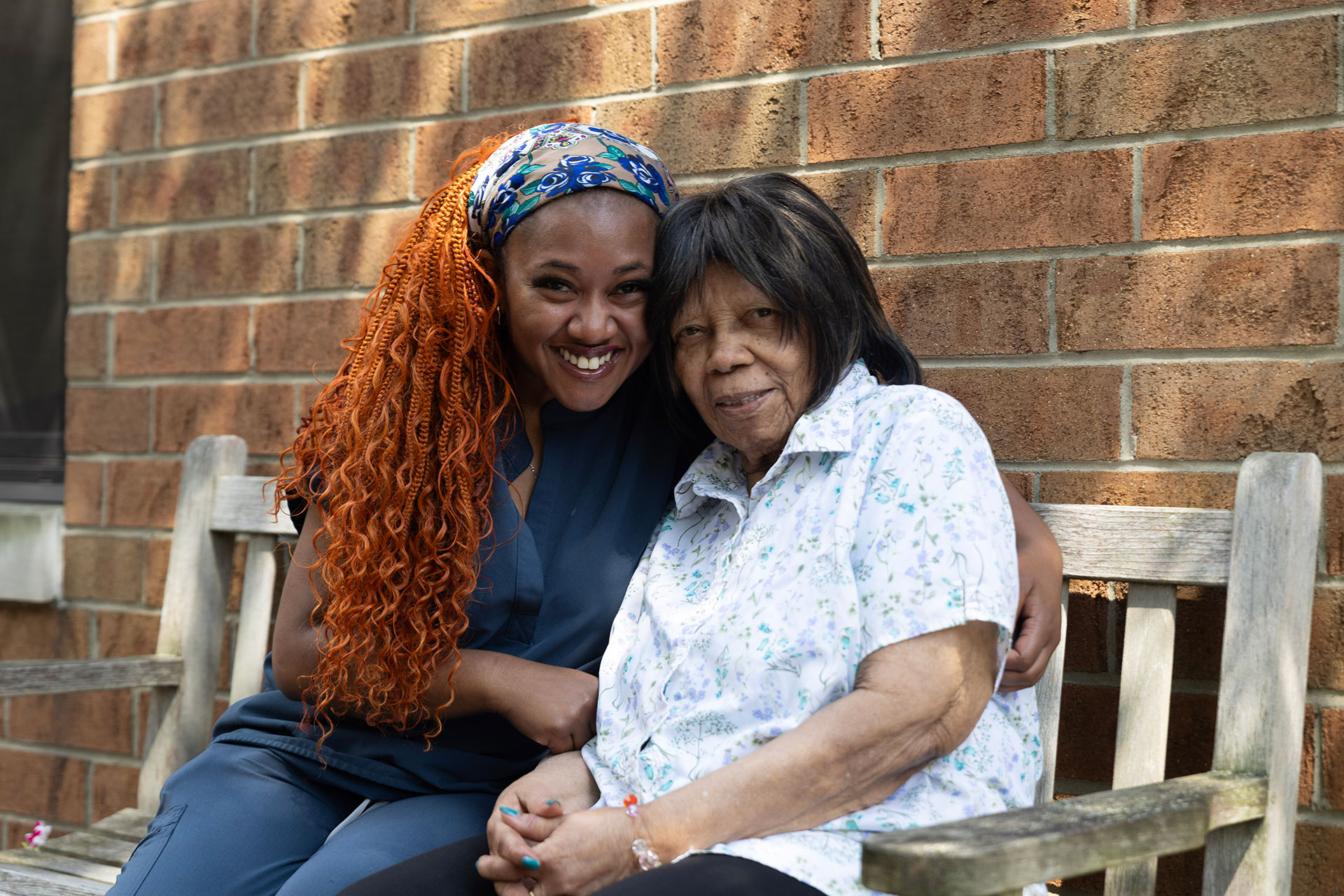 Two women smiling together on a bench, enjoying time.