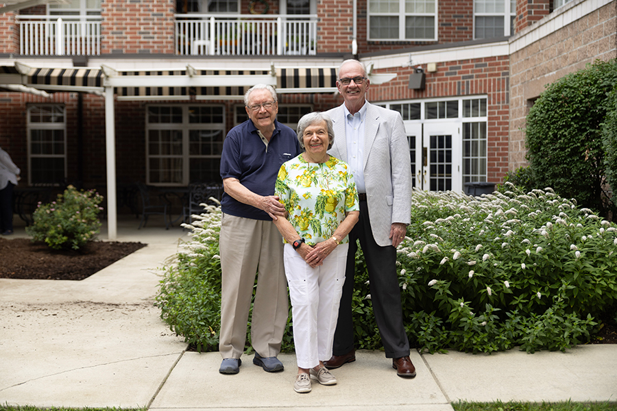Three smiling adults pose together in a garden setting.