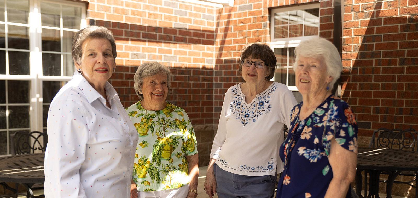 Four smiling women standing together outdoors.