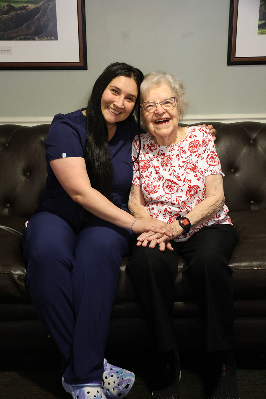 Two women smiling and holding hands on a couch.