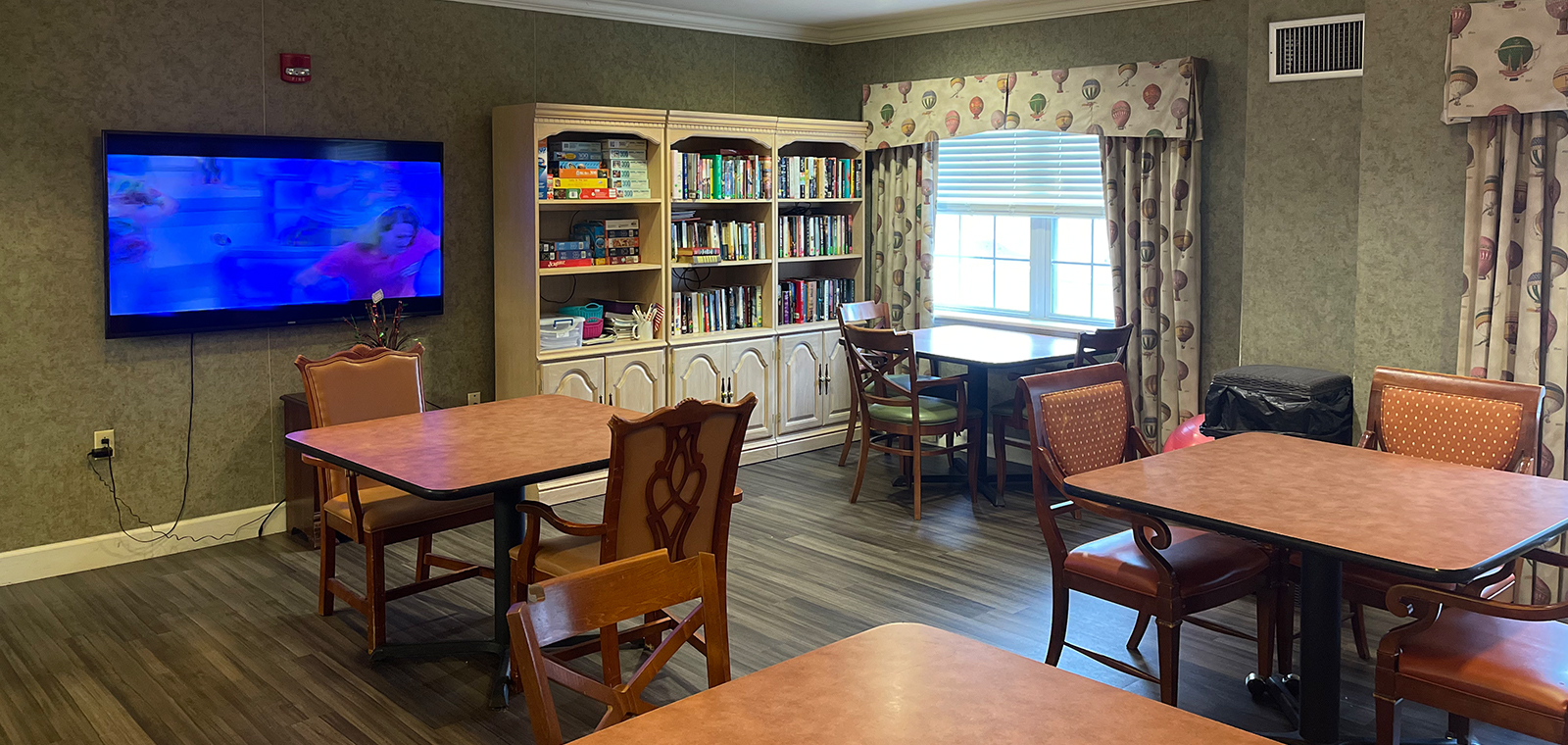 Room with tables, TV, bookshelves, and large windows.