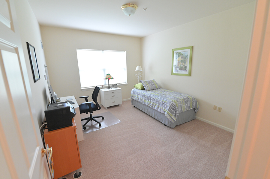 Simple bedroom with bed, desk, lamp, and window.