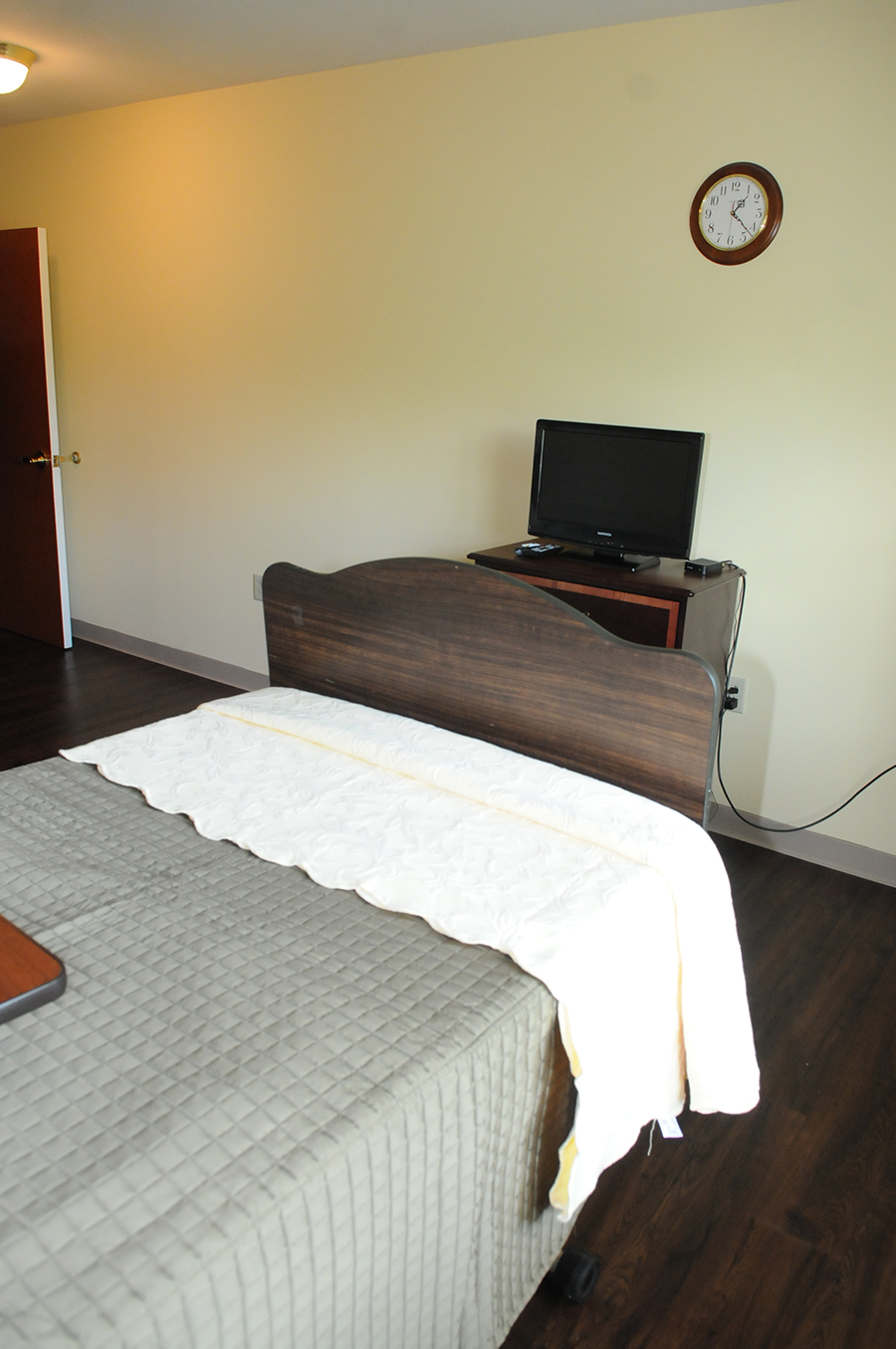Simple bedroom with a bed, television, and clock.