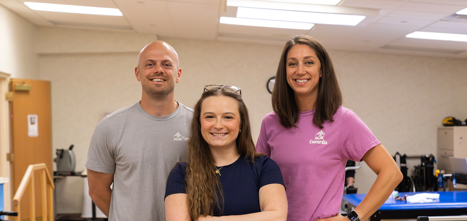 Three smiling individuals posing indoors, casual attire, friendly atmosphere.