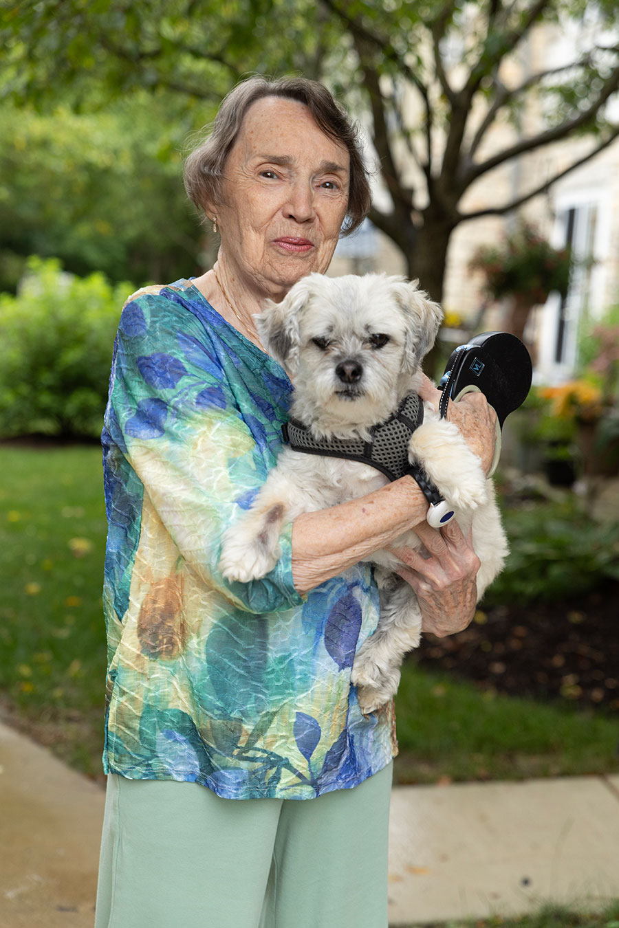 Woman holding a small dog in a garden setting.
