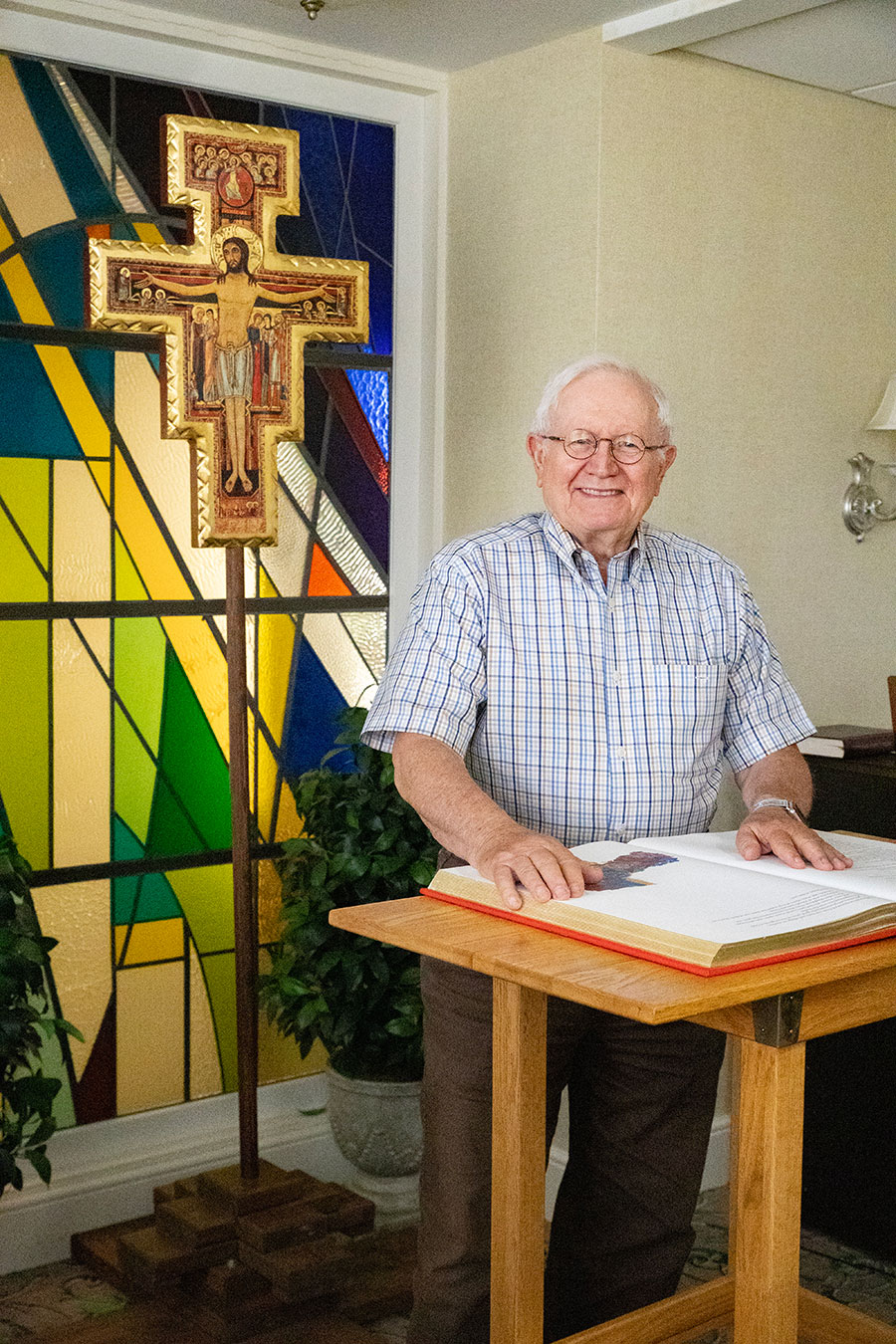 Elderly man standing by a colorful stained glass window.