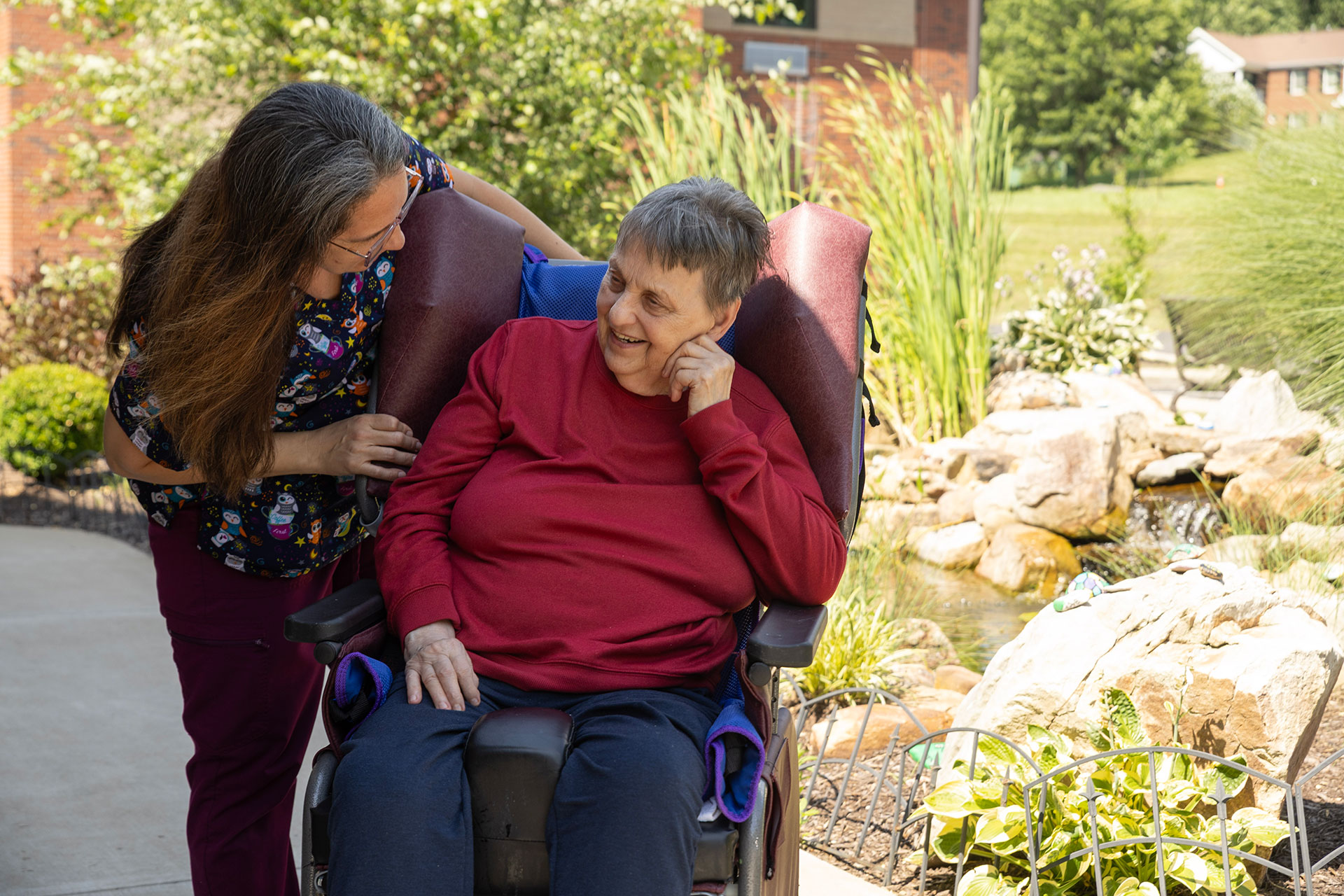A caregiver interacts warmly with a smiling elderly woman.