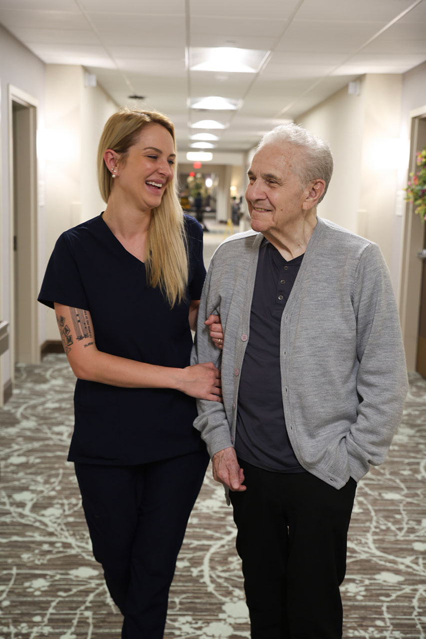 Nurse and elderly man smiling while walking together.