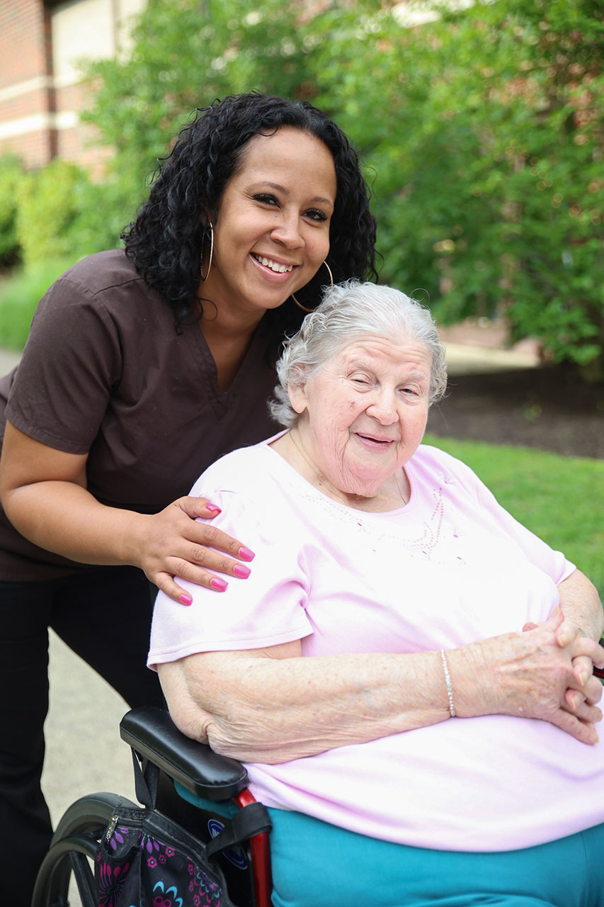 Smiling caregiver and elderly woman outside, enjoying companionship.