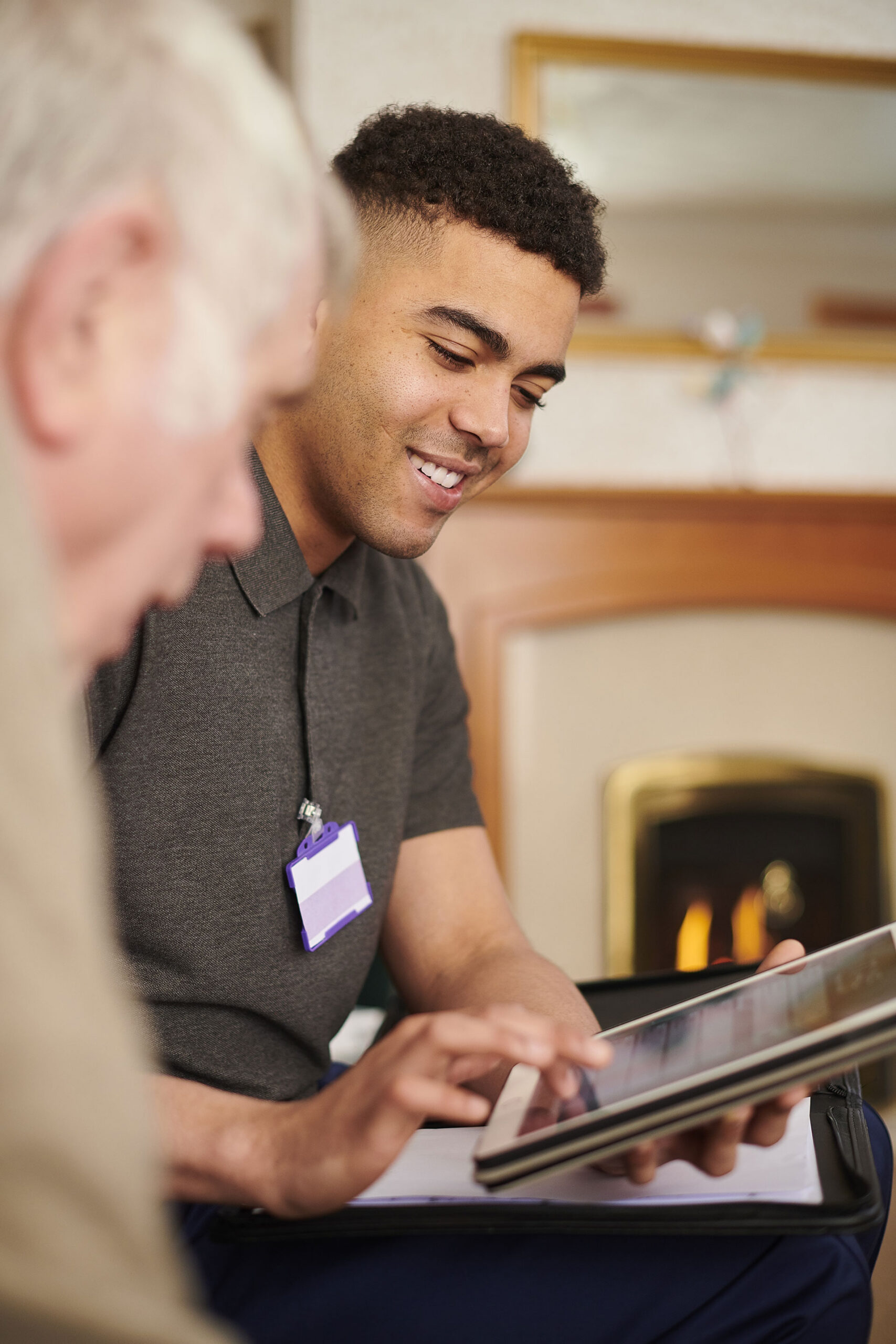 Young man using a tablet with elderly person nearby.