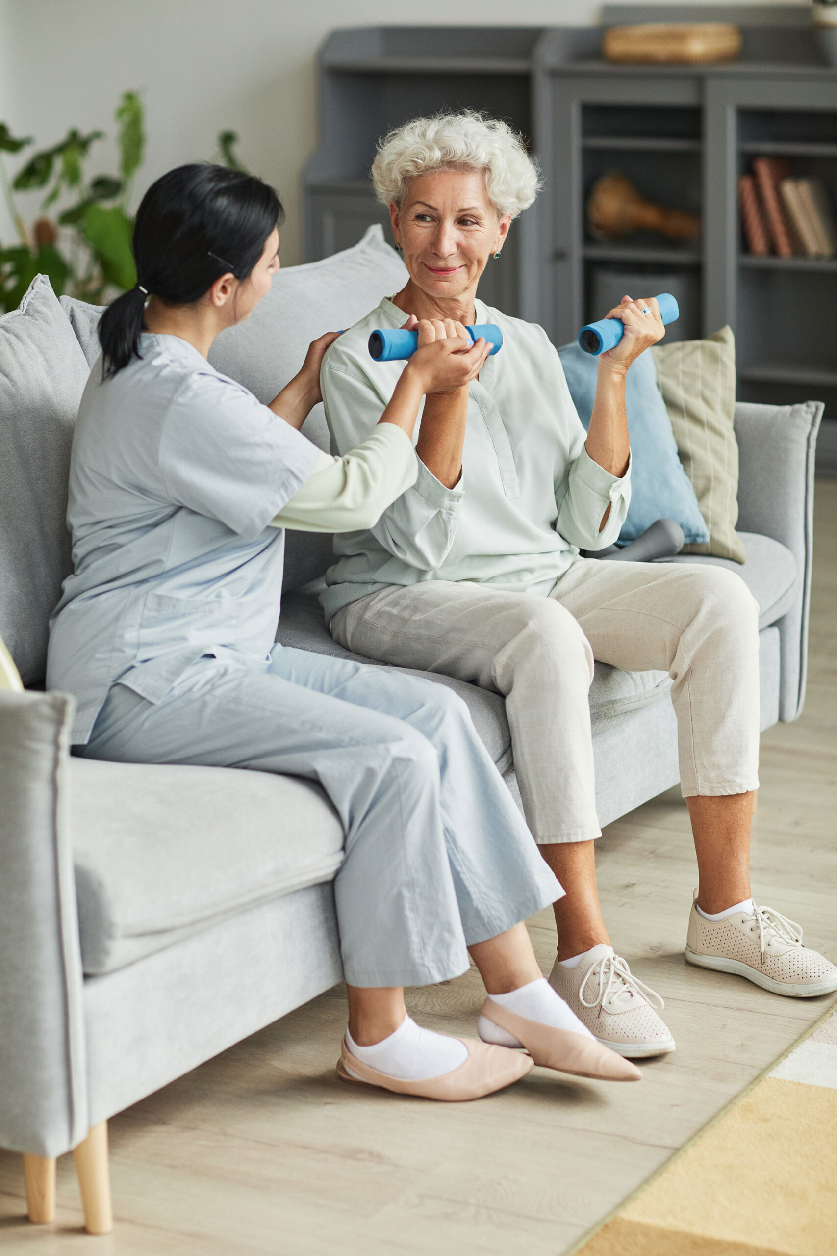 Two women exercising with dumbbells on a couch.