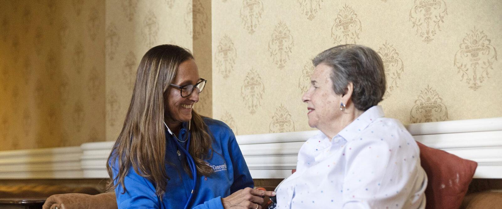 Nurse checks blood pressure of elderly woman, both smiling.