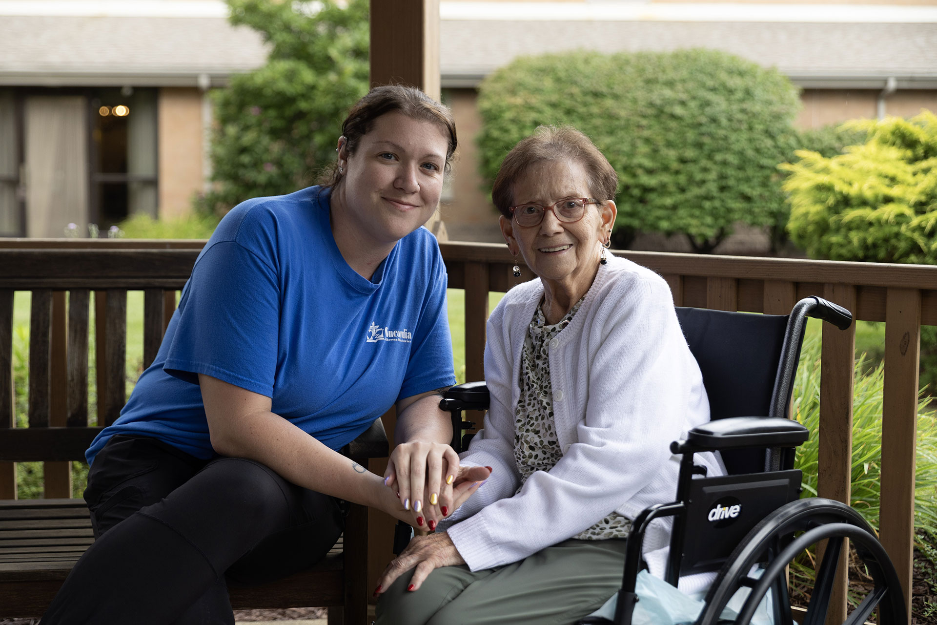 Two women smiling together on a porch, one in wheelchair.