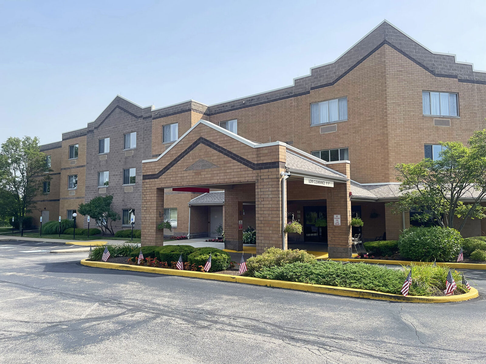 Brick building with entrance, landscaped area, and American flags.