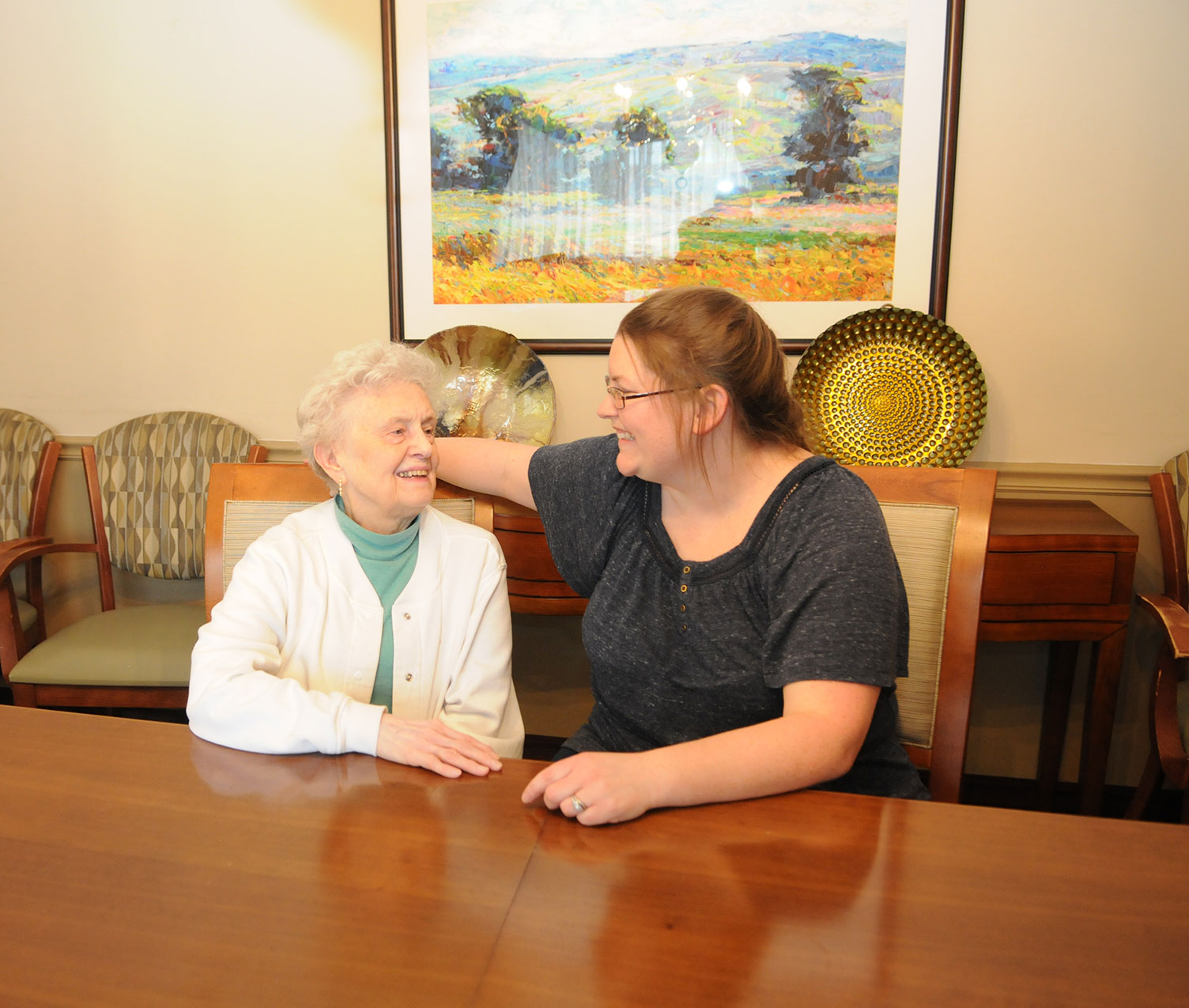 Two women sharing a smiling, intimate conversation at a table.