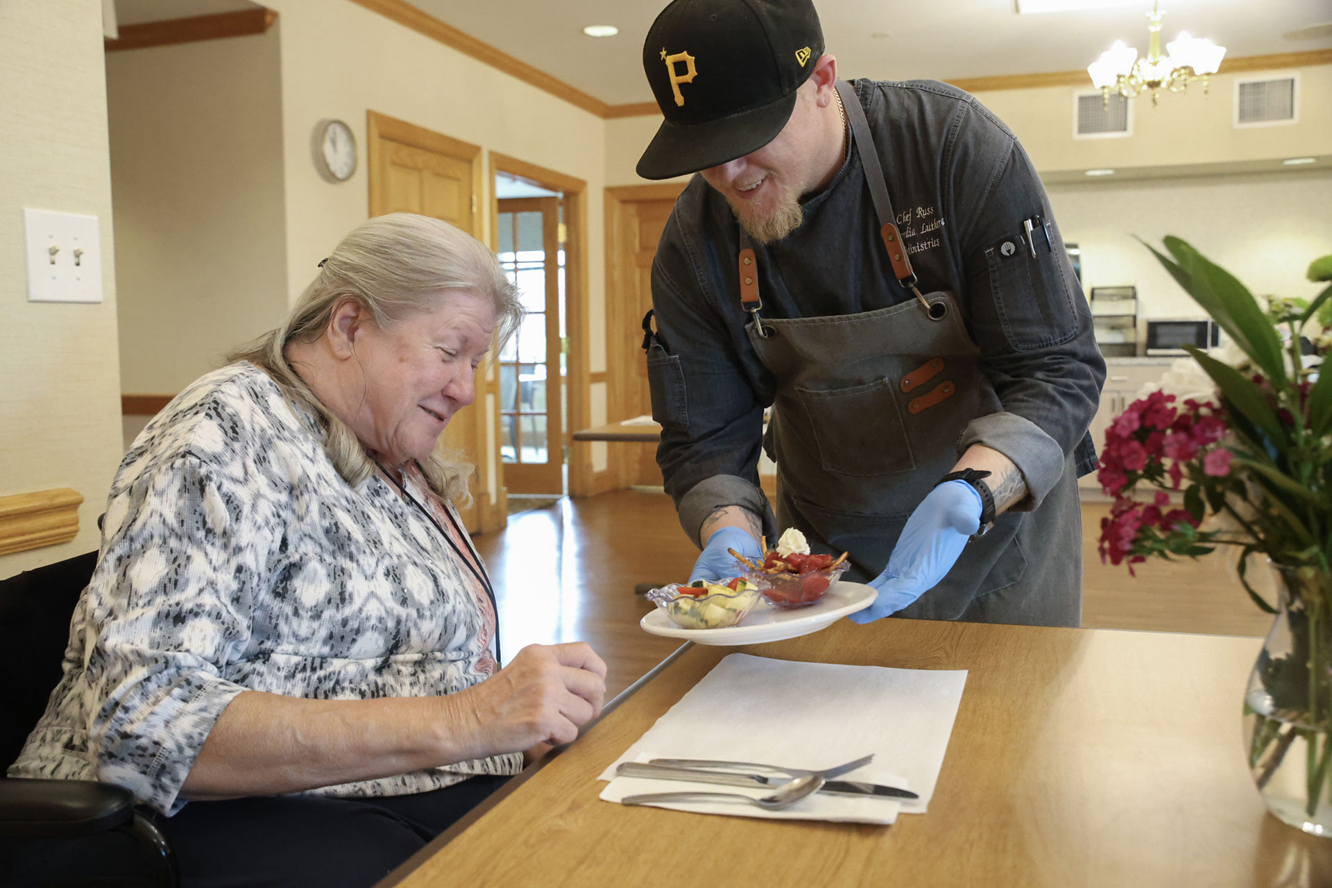 Chef serves food to a smiling woman in a dining setting.