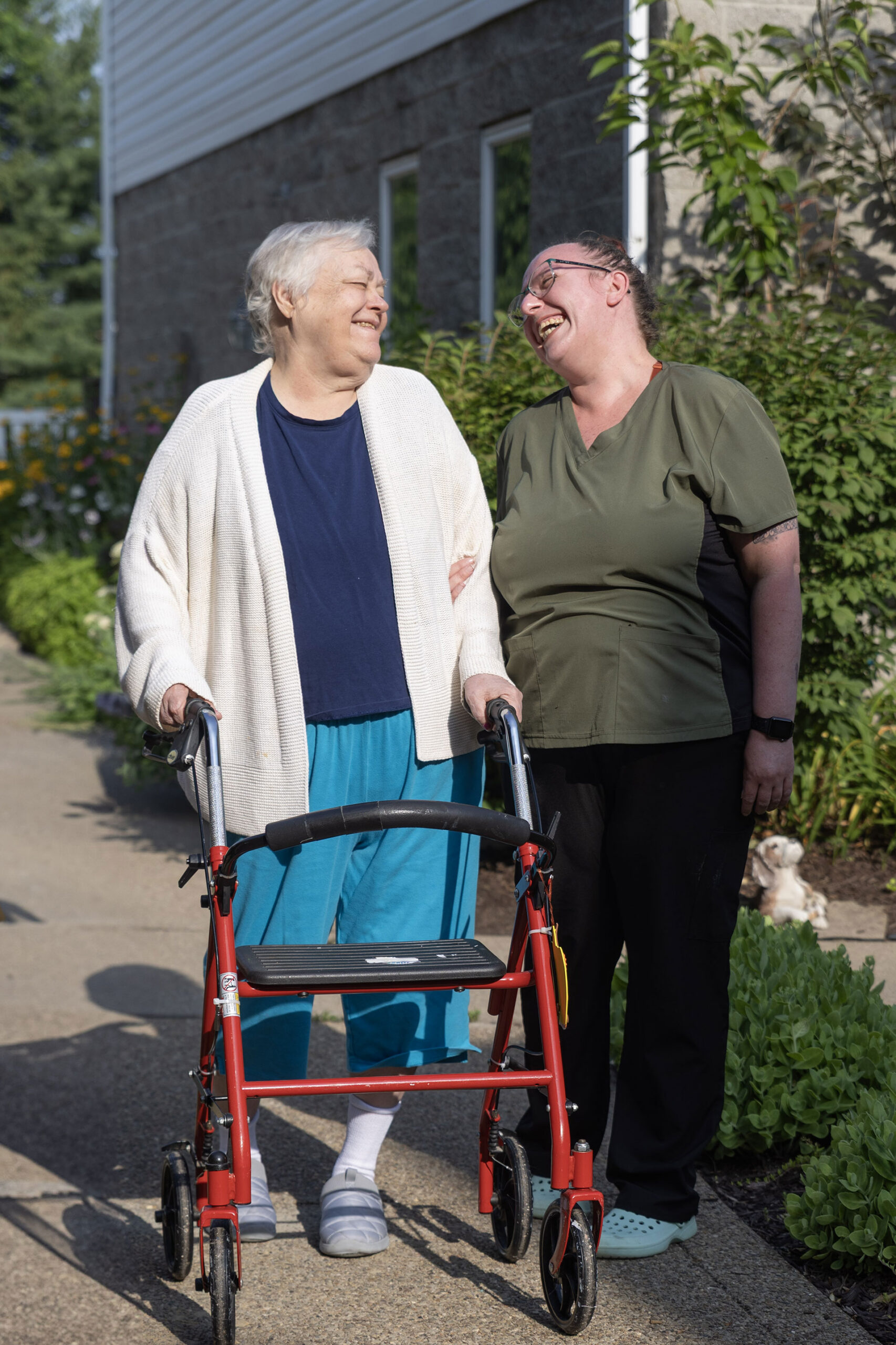 Two women laughing outdoors, one using a walker.