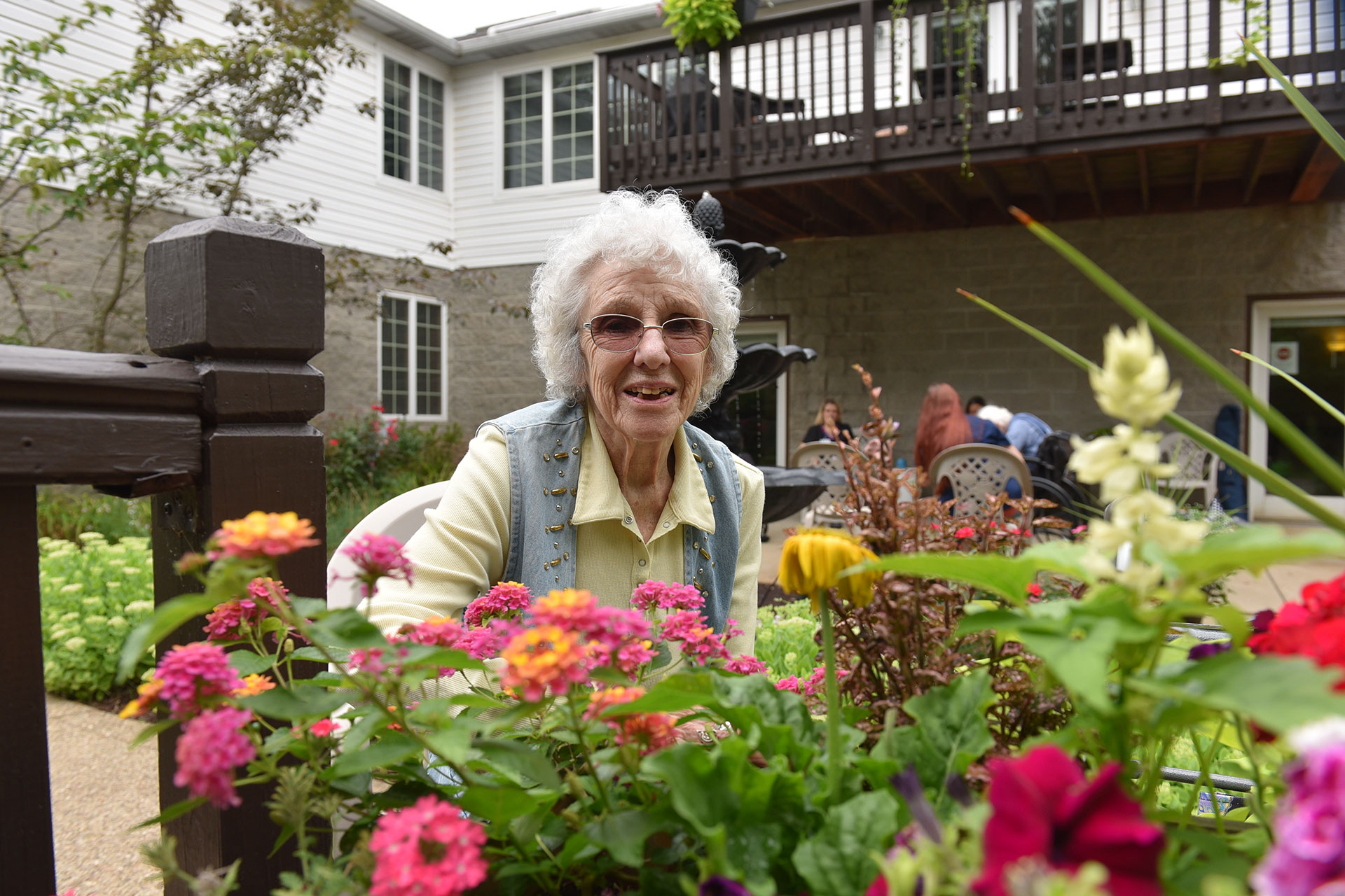 Elderly woman smiling among colorful flowers in garden setting.