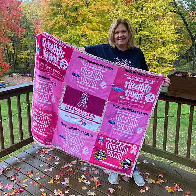 A photograph of Dawn Bastin holding a blanket made of pink terrible towels. Her late mother Phyllis made it.