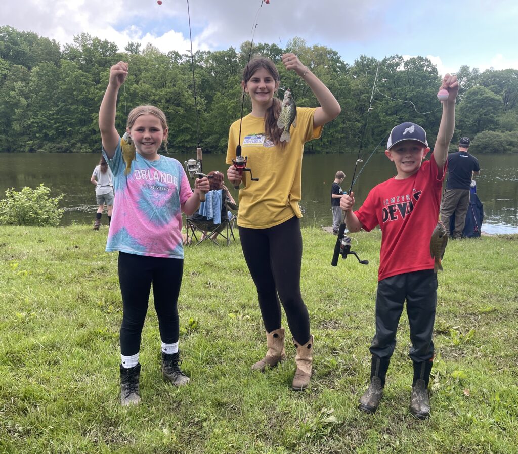 Three kids hold up fish at annual Concordia Fishing Derby