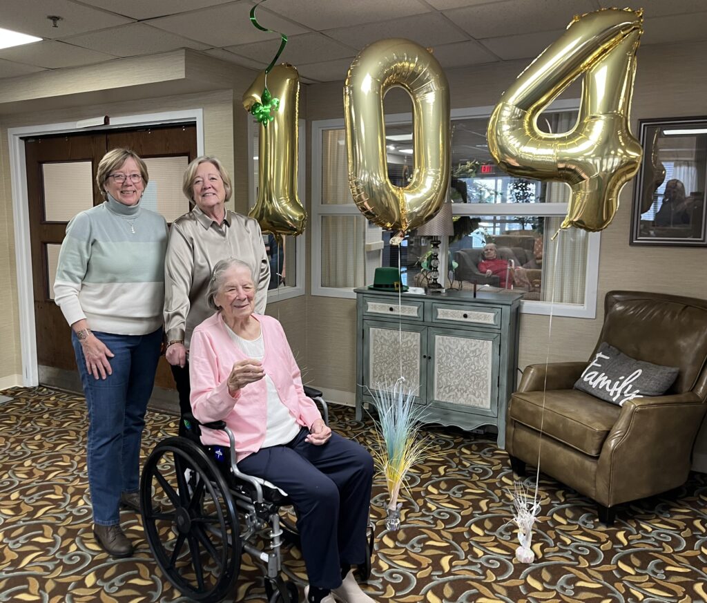 Concordia resident Julia sits in a wheelchair with her daughters Margaret and Barbara standing behind her with golden balloons in the number 104