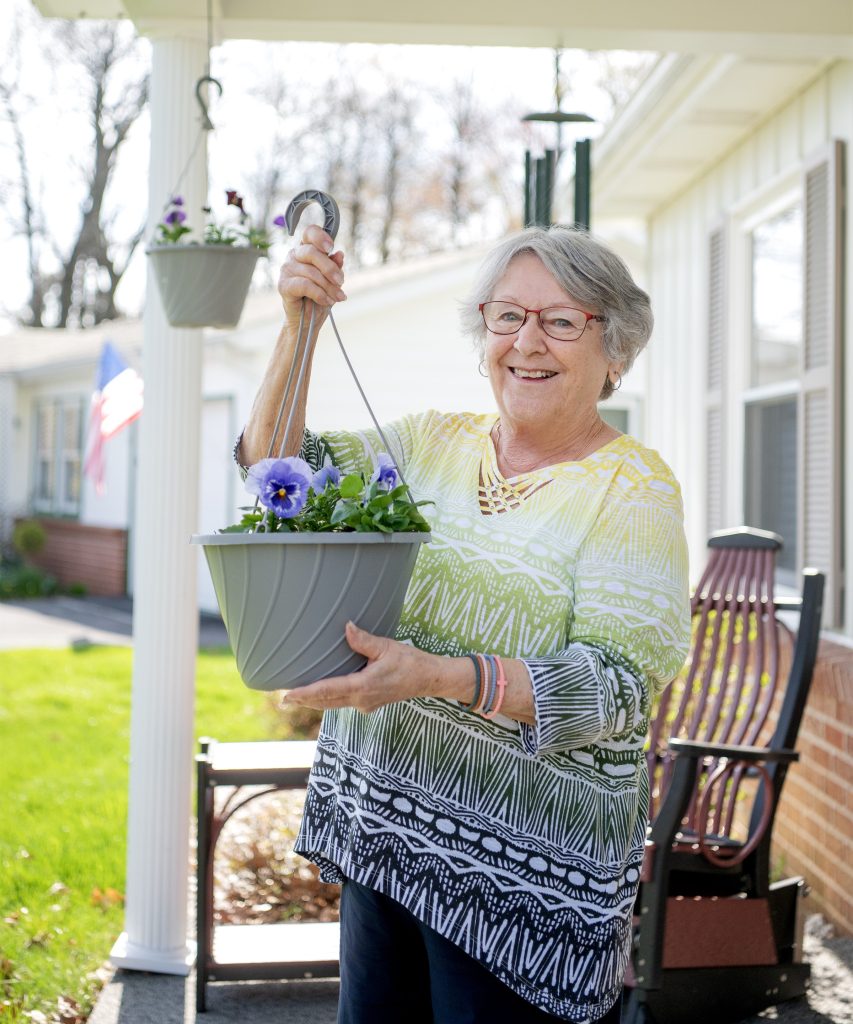 Retirement living resident hangs a potted flower basket on her porch